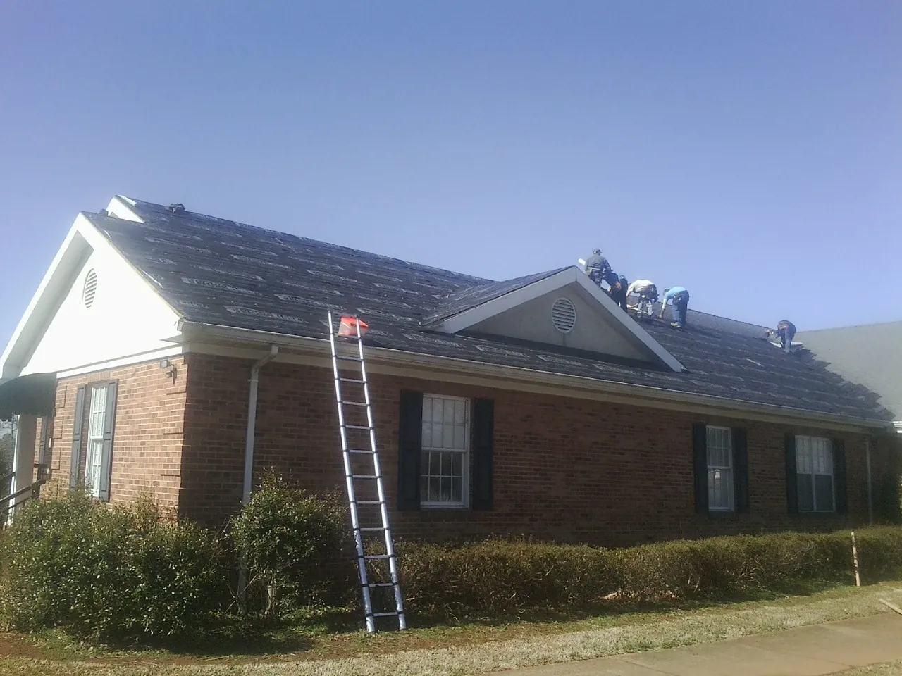 Crew tearing shingles off a brick ranch roof with a ladder set — Metal Roof Repair work by our crew in Boydton
