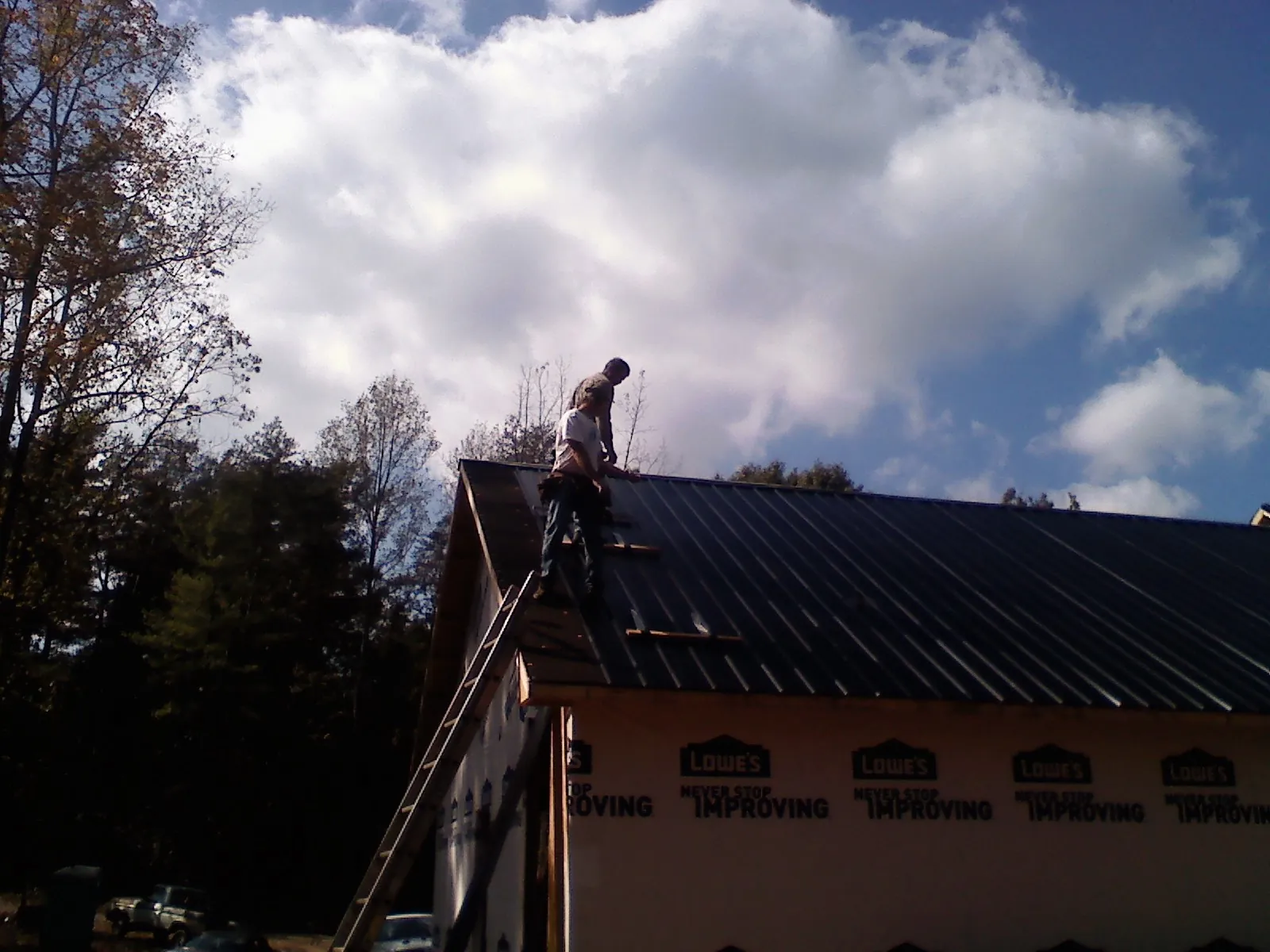 Roofer fastening dark metal panels high against a cloudy sky, from a Roof Inspection job in Boydton