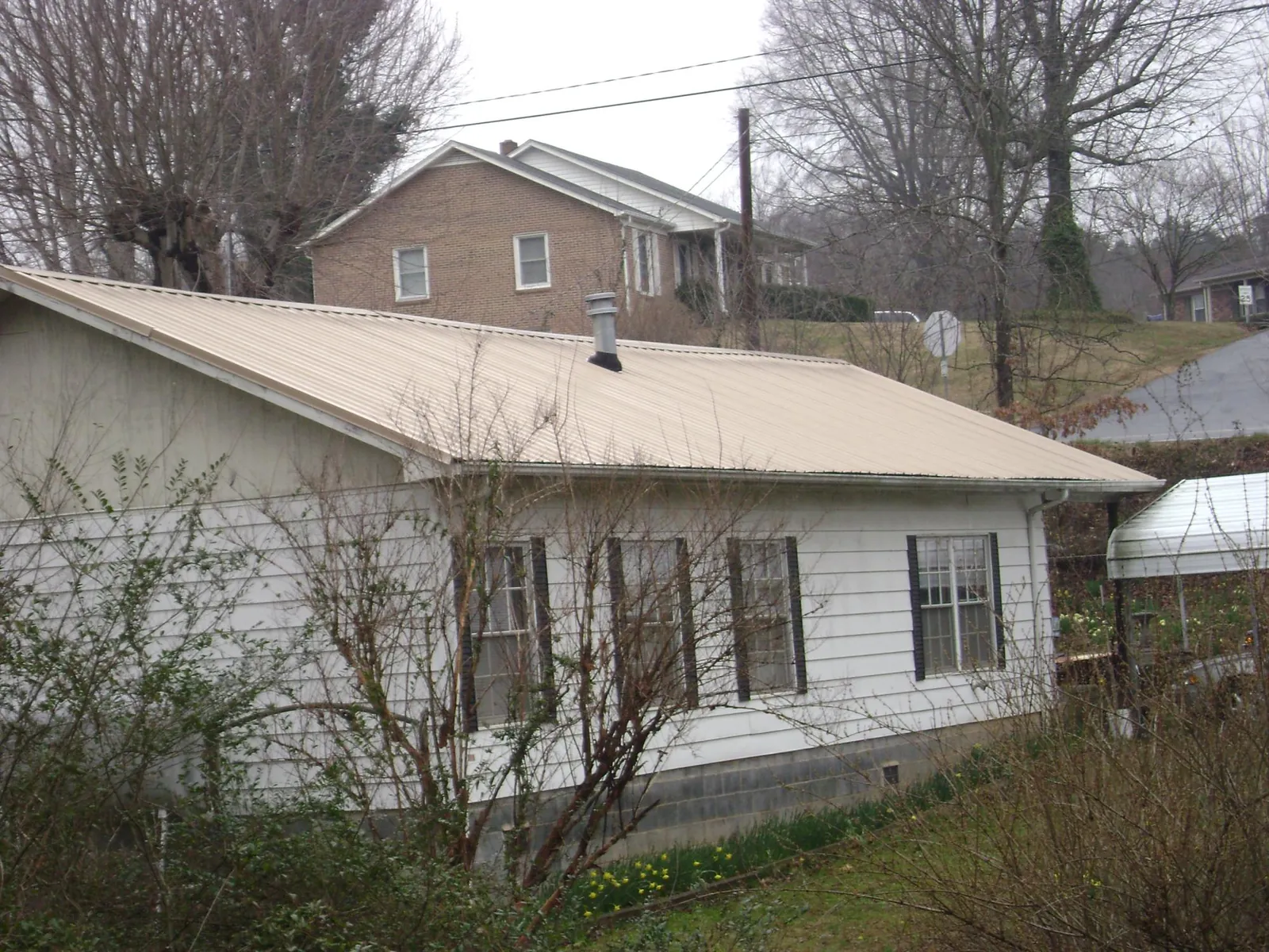 Tan metal roof on a white sided house set into a hillside — Commercial Roofing by Roofing Brothers in Boydton